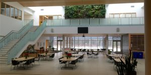 Verschuren Centre Atrium is open venue with brown floor and white ceilings having tables with chairs and stairs to go to second level floor